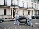 Two men walking a Spit Roast machine across a street
