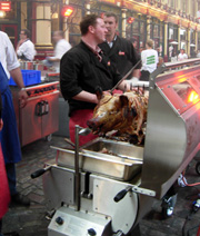 Man at a city event roasting a hog on a spit